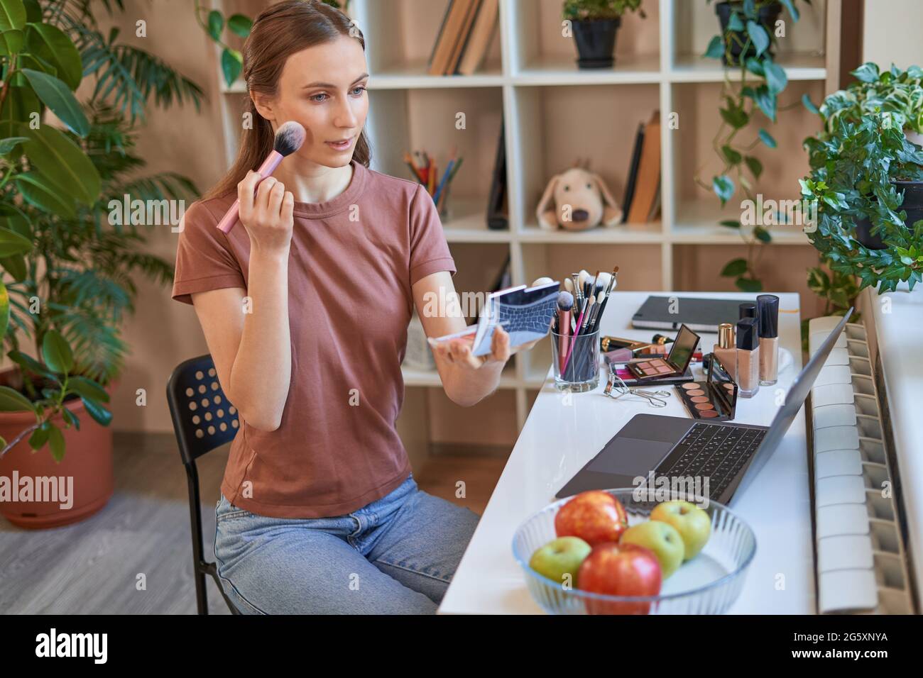 Sorridente signora attraente usando i cosmetici mentre imparando in linea Foto Stock
