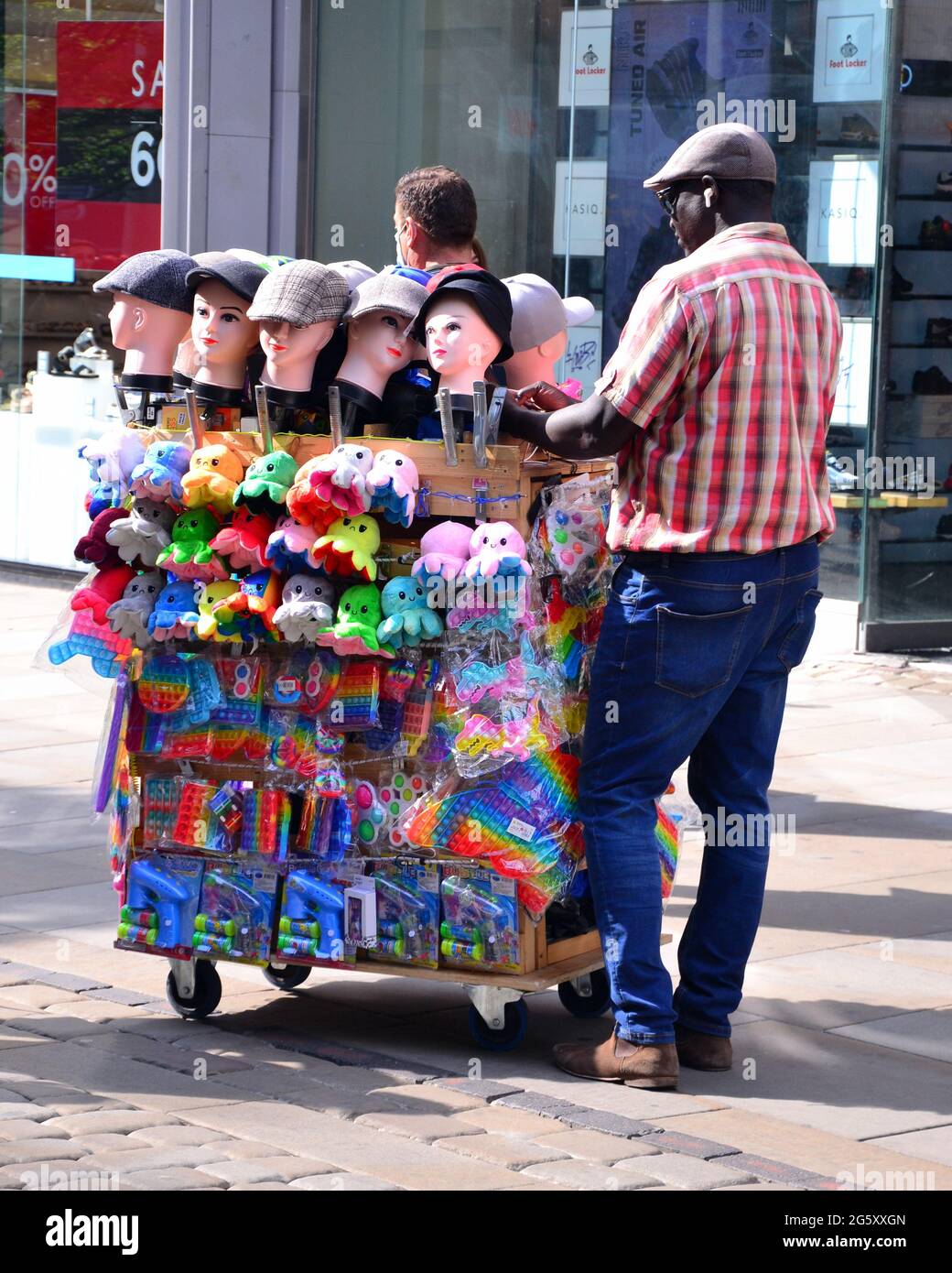 Man spinge il carrello che vende cappelli e giocattoli nel centro di Manchester, Inghilterra, Regno Unito, Foto Stock