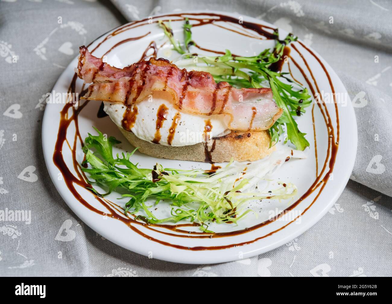 Deliziosa colazione leggera con uova in camicia su bruschetta con pancetta, insalata di fregi e condimento con salsa balsamica. Foto Stock