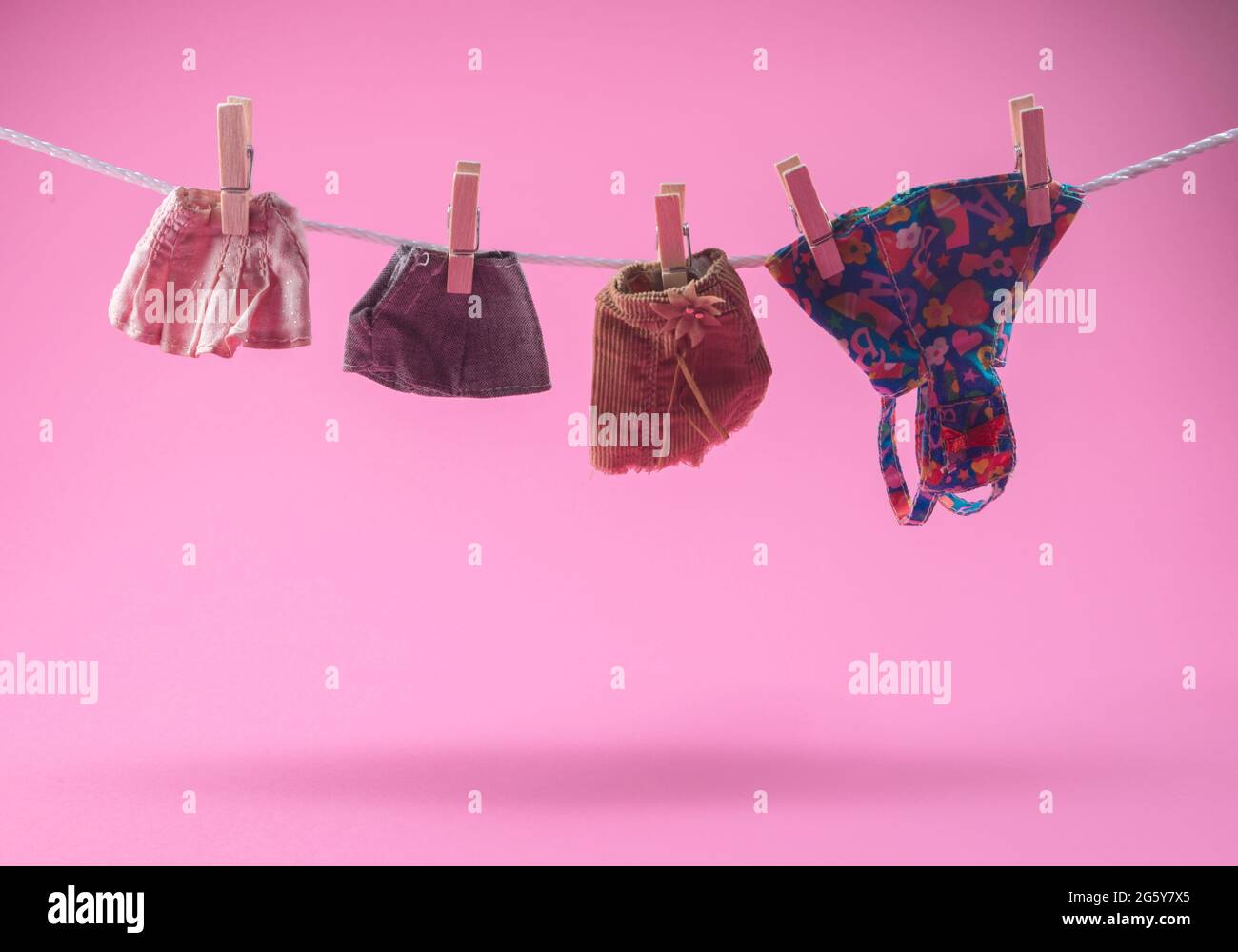 Gonne di moda e abito appeso su una corda con i pioli. Su sfondo rosa pastello alla moda. Giocattoli per bambini piccoli vestiti per bambole. Concetto costoso. Foto Stock