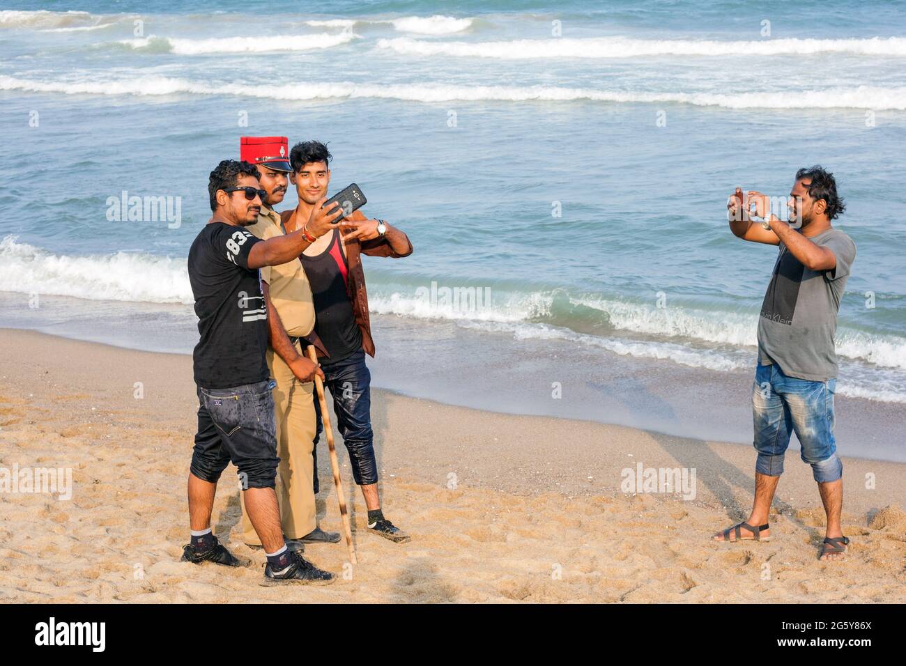 L'ufficiale di polizia di Puducherry che indossa il kepi francese e trasporta il lathi pone per i selfie con i turisti indiani, Puducherry (Pondicherry), Tamil Nadu, India Foto Stock