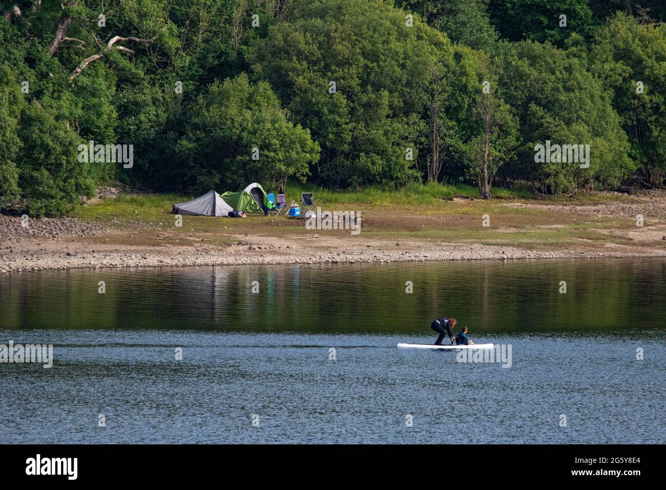 Loch Venachar, Loch. Lomonnd e Trossachs National Park, Scozia, Regno Unito. 30 giugno 2021. NELLA FOTO: Le tende si accopicchiano sul lato del lago e la gente fuori sull'acqua paddle boarding, kayak, nuoto selvaggio e godendo il caldo tempo estivo durante un tempo in cui i laghi scozzesi sono esauriti di acqua. La grande spiaggia di stoney è rivelata intorno al lago che normalmente sarebbe completamente sotto l'acqua ma con il tempo asciutto e caldo lungo non ci è niente sostituire l'acqua che evapora. Credit: Colin Fisher/Alamy Live News Foto Stock