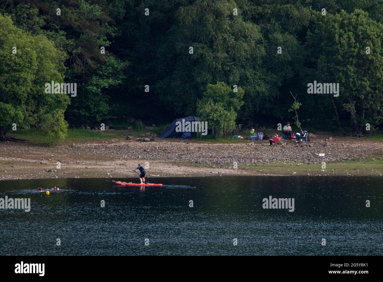 Loch Venachar, Loch. Lomonnd e Trossachs National Park, Scozia, Regno Unito. 30 giugno 2021. NELLA FOTO: Le persone che si trovano sull'acqua possono fare paddle boarding, kayak, nuoto selvaggio e godersi il caldo clima estivo durante un periodo in cui i laghi scozzesi sono impoveriti di acqua. La grande spiaggia di stoney è rivelata intorno al lago che normalmente sarebbe completamente sotto l'acqua ma con il tempo asciutto e caldo lungo non ci è niente sostituire l'acqua che evapora. Credit: Colin Fisher/Alamy Live News Foto Stock