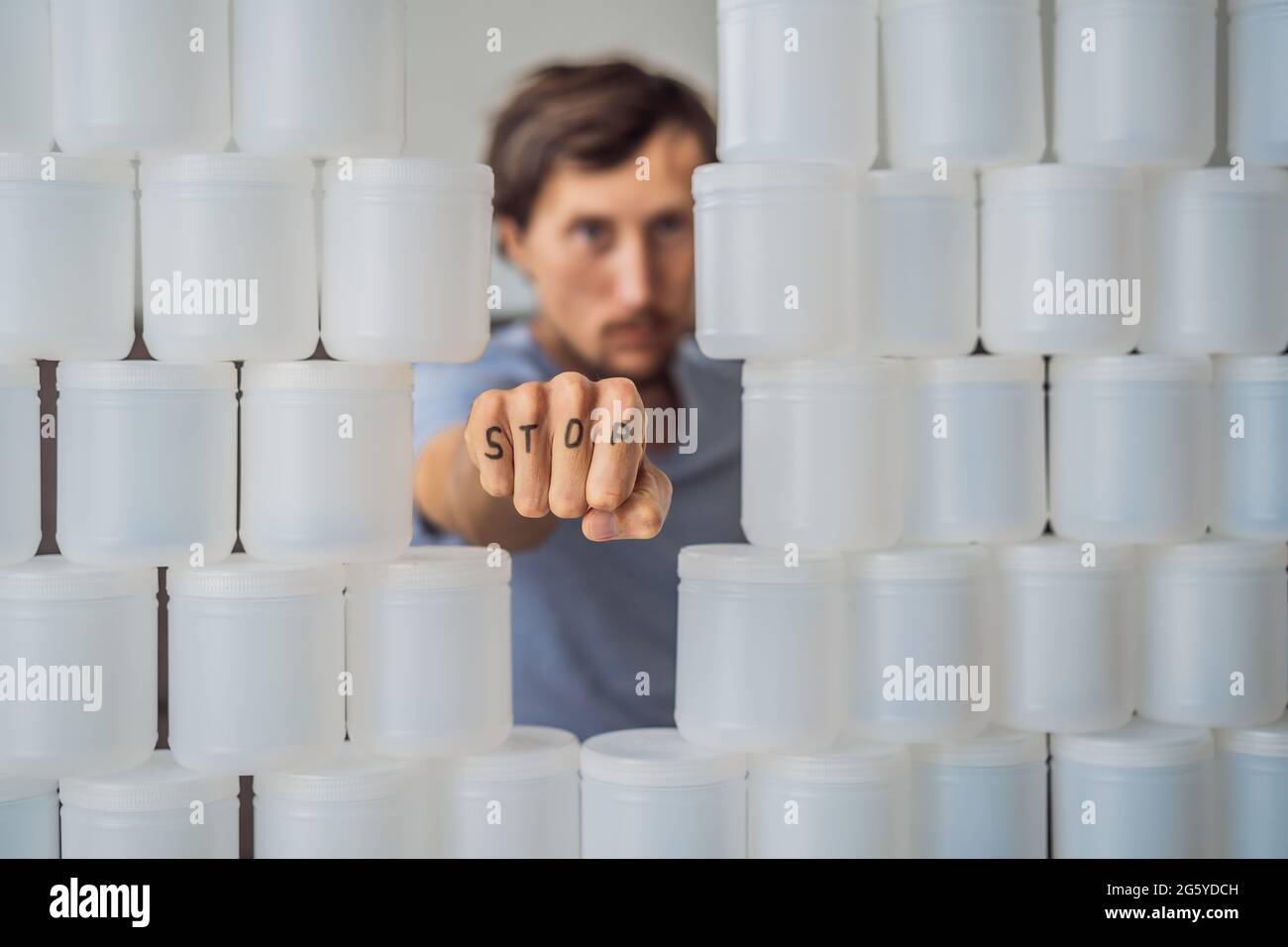 Uomo che mostra stop circondato da molti vasi di yogurt che usa in un anno. Una grande quantità di vasetti di plastica per alimenti. Consumo eccessivo di plastica Foto Stock