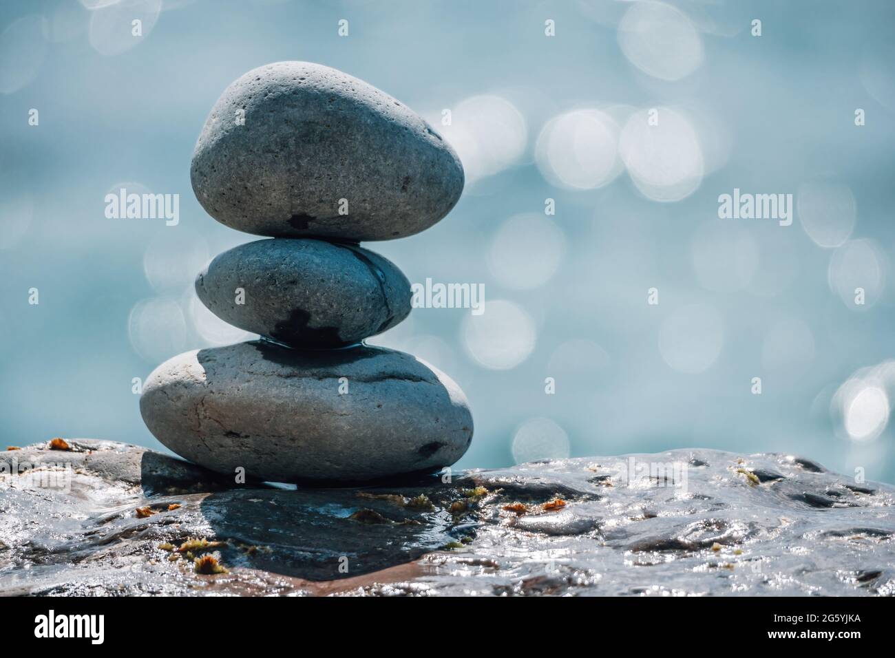 Equilibrata piramide di ciottoli sulla spiaggia in una giornata di sole. Abstract Sea bokeh sullo sfondo. Messa a fuoco selettiva. Pietre Zen sulla spiaggia di mare, meditazione Foto Stock