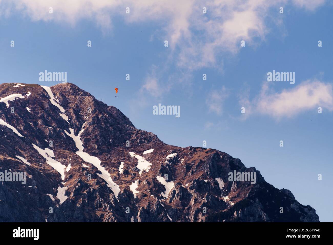 Vetta di montagna con chiazze di neve e parapendio volare sopra. Alpinismo, sport estremi e concetti naturalistici. Foto Stock