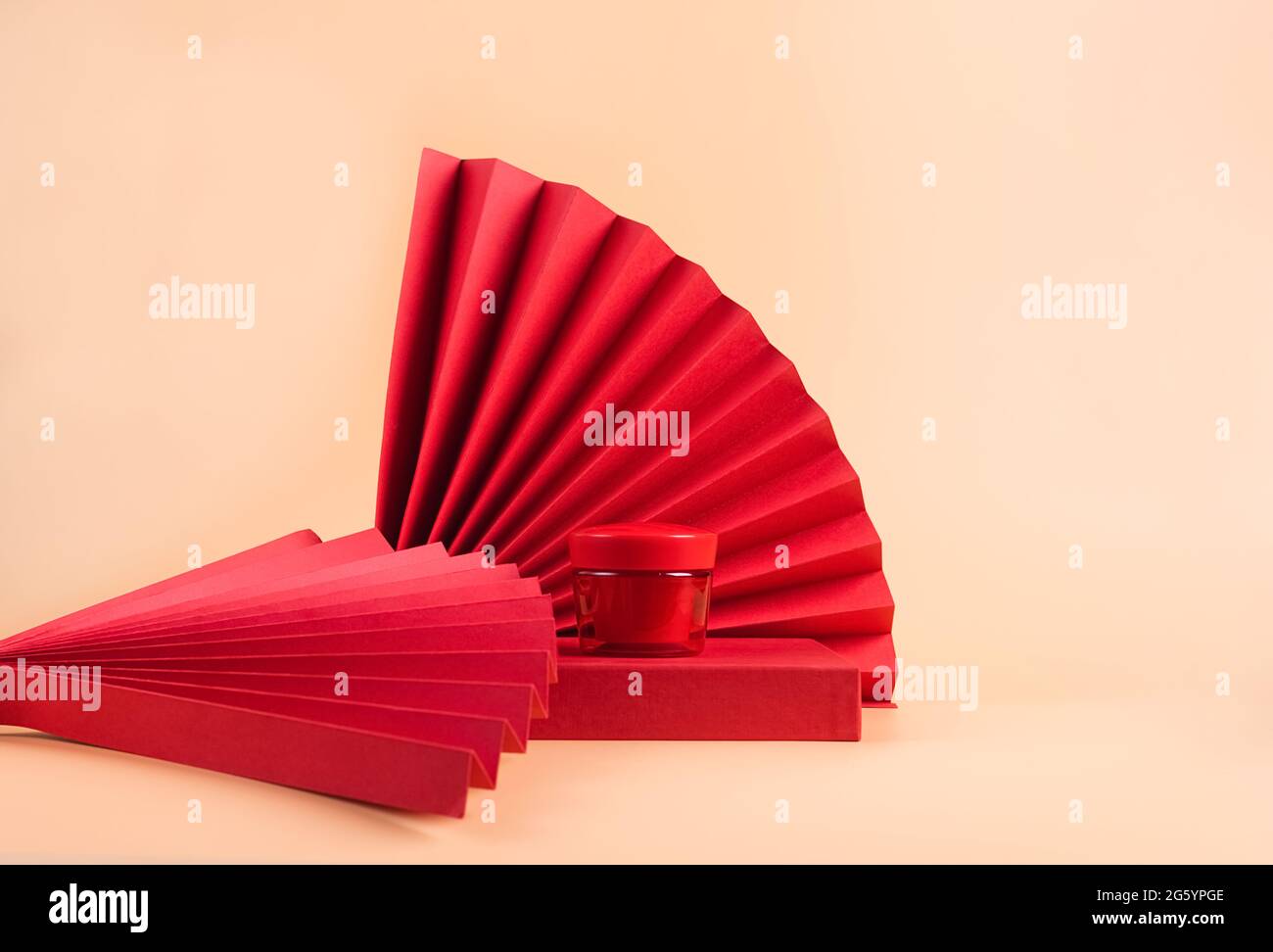 Crema cosmetica in un vaso rosso si erge su un podio rosso carta orientale ventilatore fioritura ramo con gemme rosa pastello sfondo Foto Stock