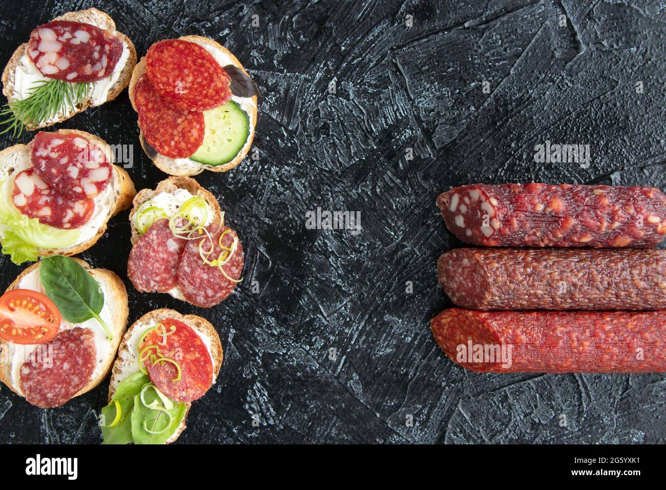 vista dall'alto su sei panini o spuntini con salsicce e tre tipi di salsicce diverse su sfondo nero. posa piatta. Messa a fuoco morbida. Foto Stock