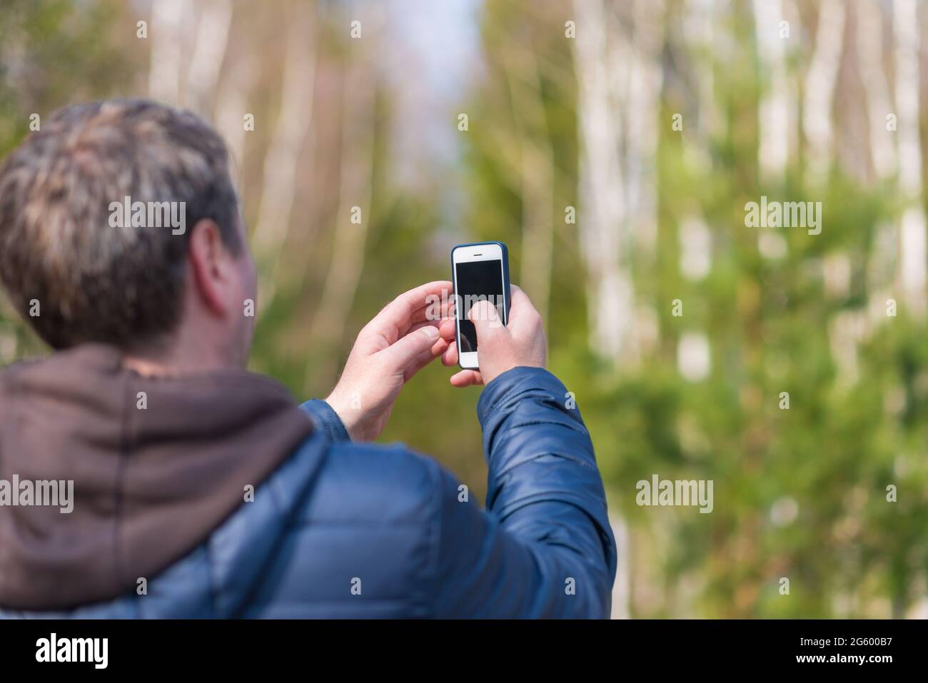 Un uomo di 40 anni con il suo smartphone cellulare alla ricerca del segnale di ricezione nella foresta primaverile. Foto Stock
