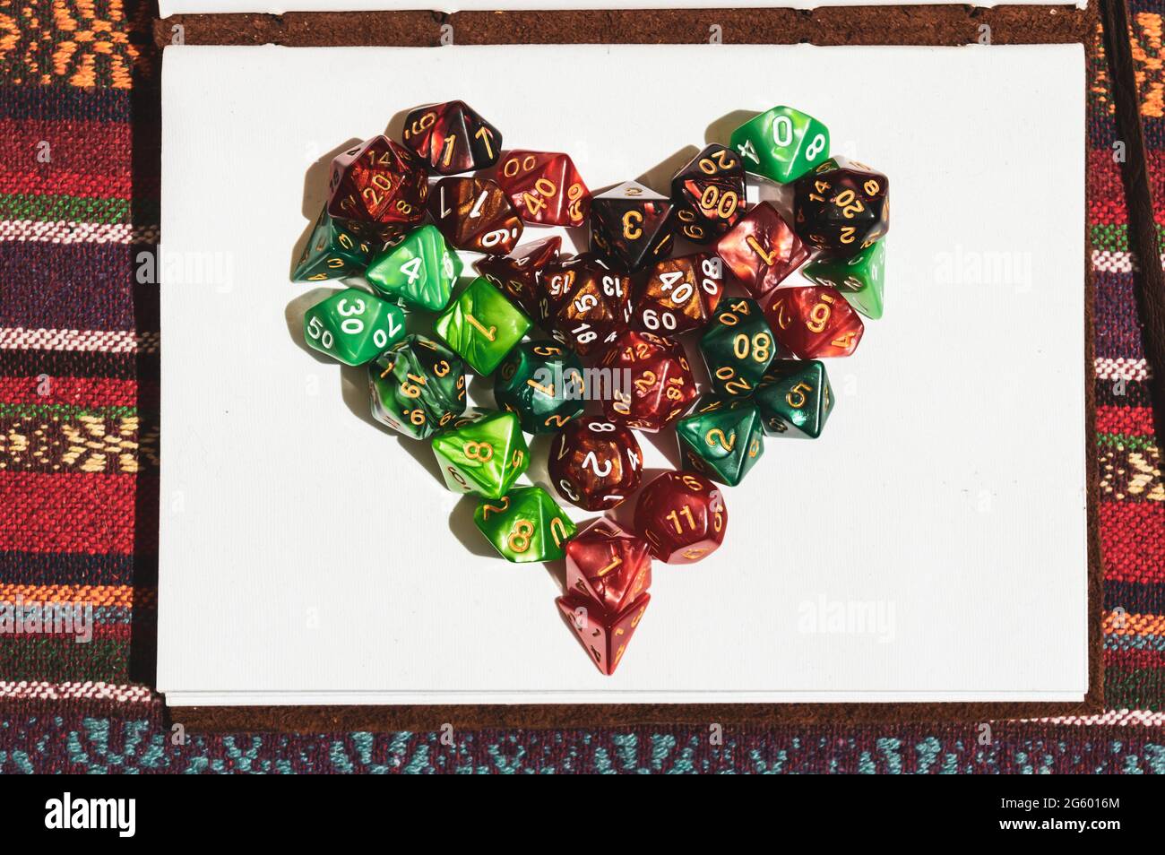 Immagine di un simbolo del cuore creato con dadi di gioco di ruolo verdi e rossi sulla parte superiore di un notebook aperto al sole Foto Stock