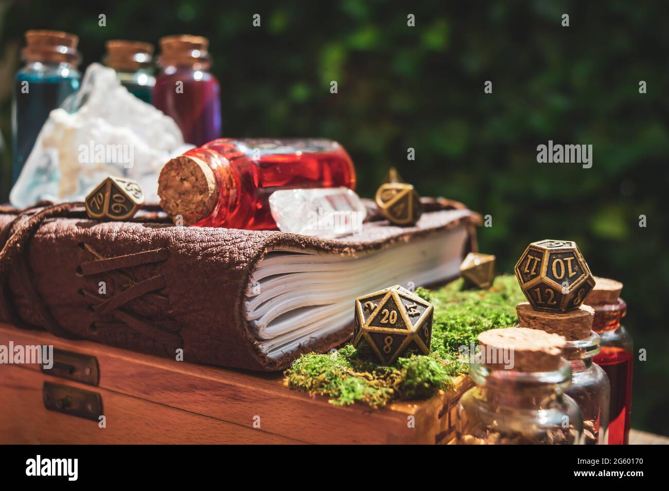 Primo piano di un dado metallizzato di gioco di ruolo a 20 lati accanto a un libro in pelle, bottiglie di pozione e cristalli al sole Foto Stock