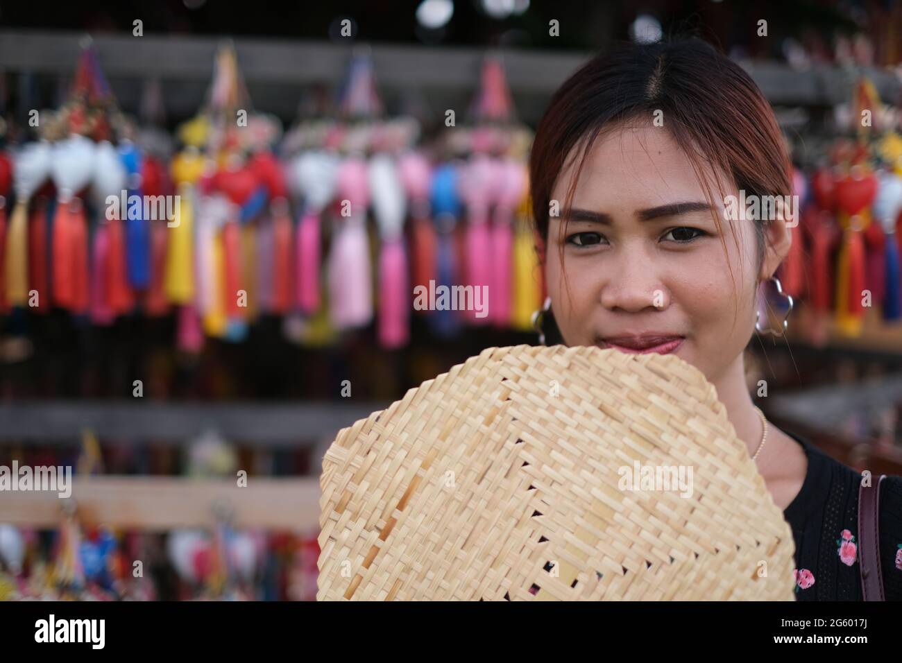 Attraente donna tailandese copre il suo viso con un tradizionale ventilatore di bambù, in piedi di fronte alla fila di colorati pendenti in stile cinese Foto Stock