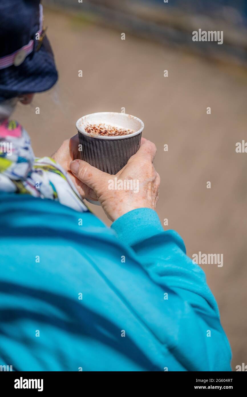 Una persona anziana che tiene un caffè cappuccino in una tazza monouso. Foto Stock