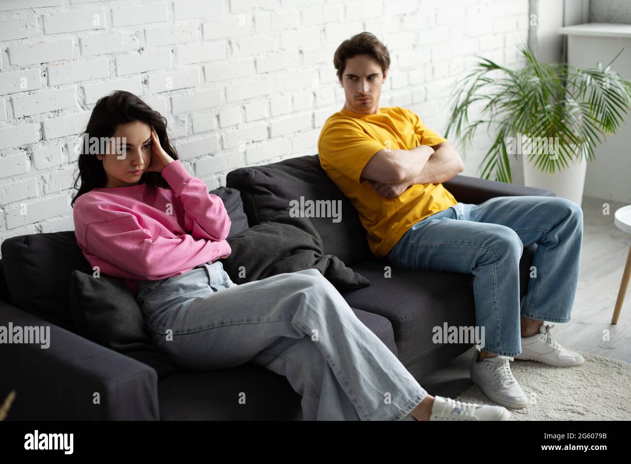 giovane arrabbiato con le braccia incrociate seduti sul divano e guardando la ragazza con la mano vicino alla testa in soggiorno Foto Stock