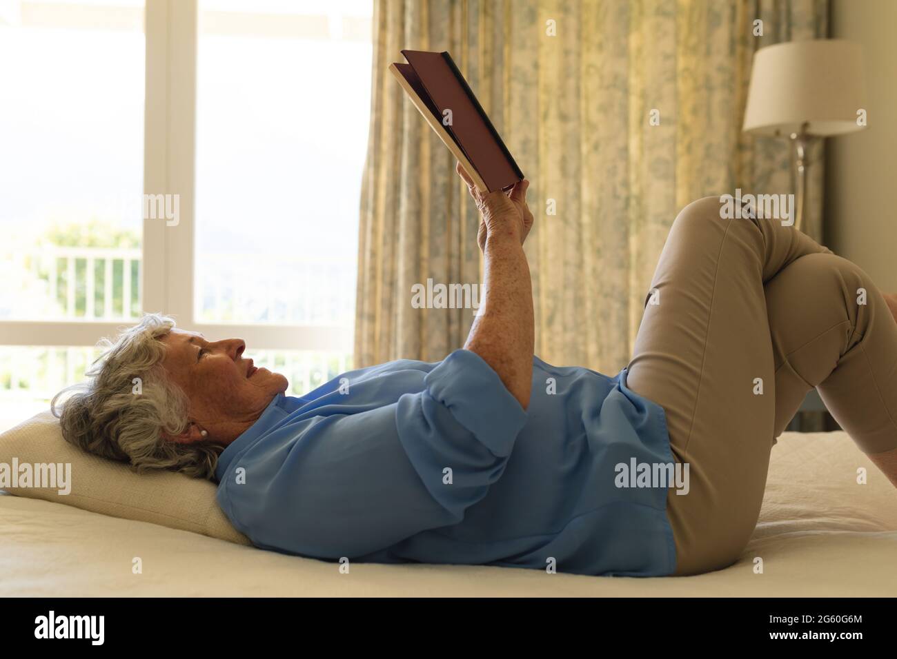 Donna caucasica anziana sdraiata in letto e leggere libro in camera da letto Foto Stock