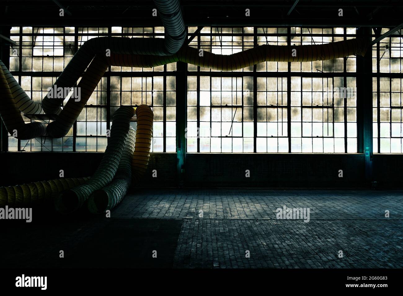 Le vecchie finestre della fabbrica erano sporche, con pavimento in mattoni e duttwork Foto Stock