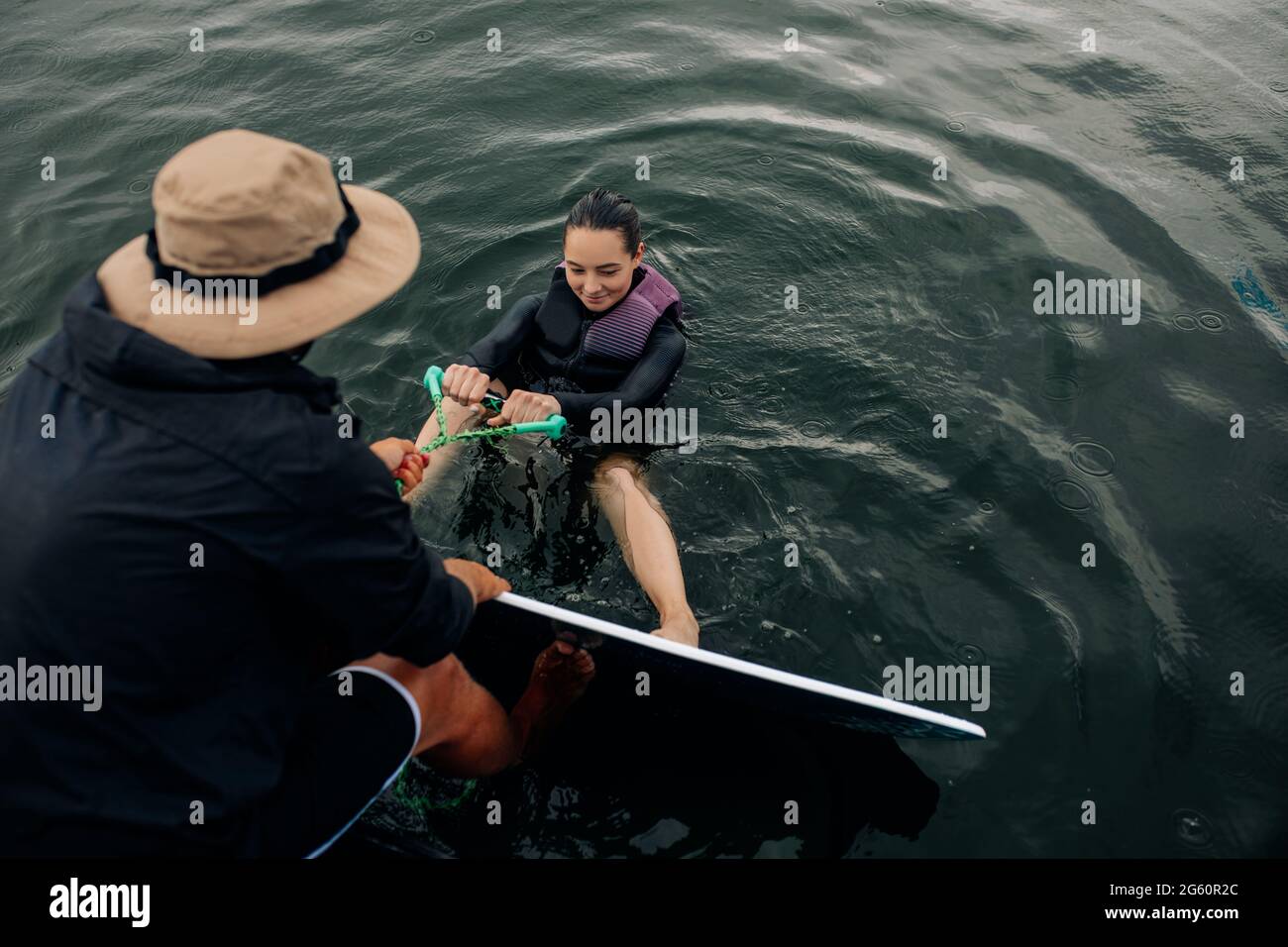L'istruttore insegna la tecnica di wakesurf della giovane donna e impara come alzarsi in piedi sulla tavola da surf mentre tiene la corda di traino. Foto Stock