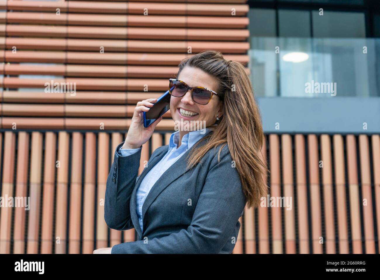 Felice elegante donna di affari sorridente e guardando la macchina fotografica che chiama dal telefono. Foto Stock