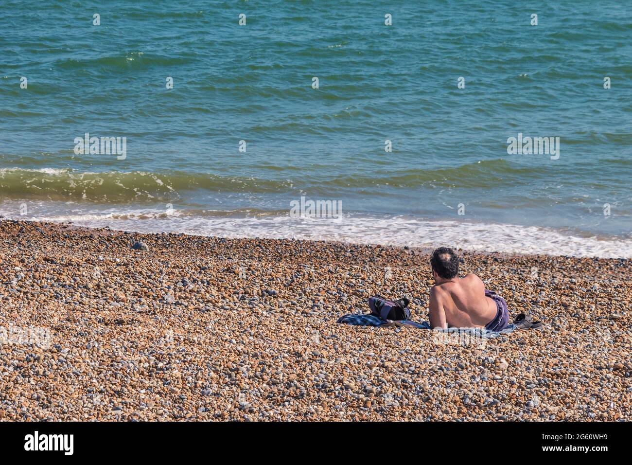 Un uomo seduto sulla spiaggia in una giornata calda a Hastings, Regno Unito Foto Stock