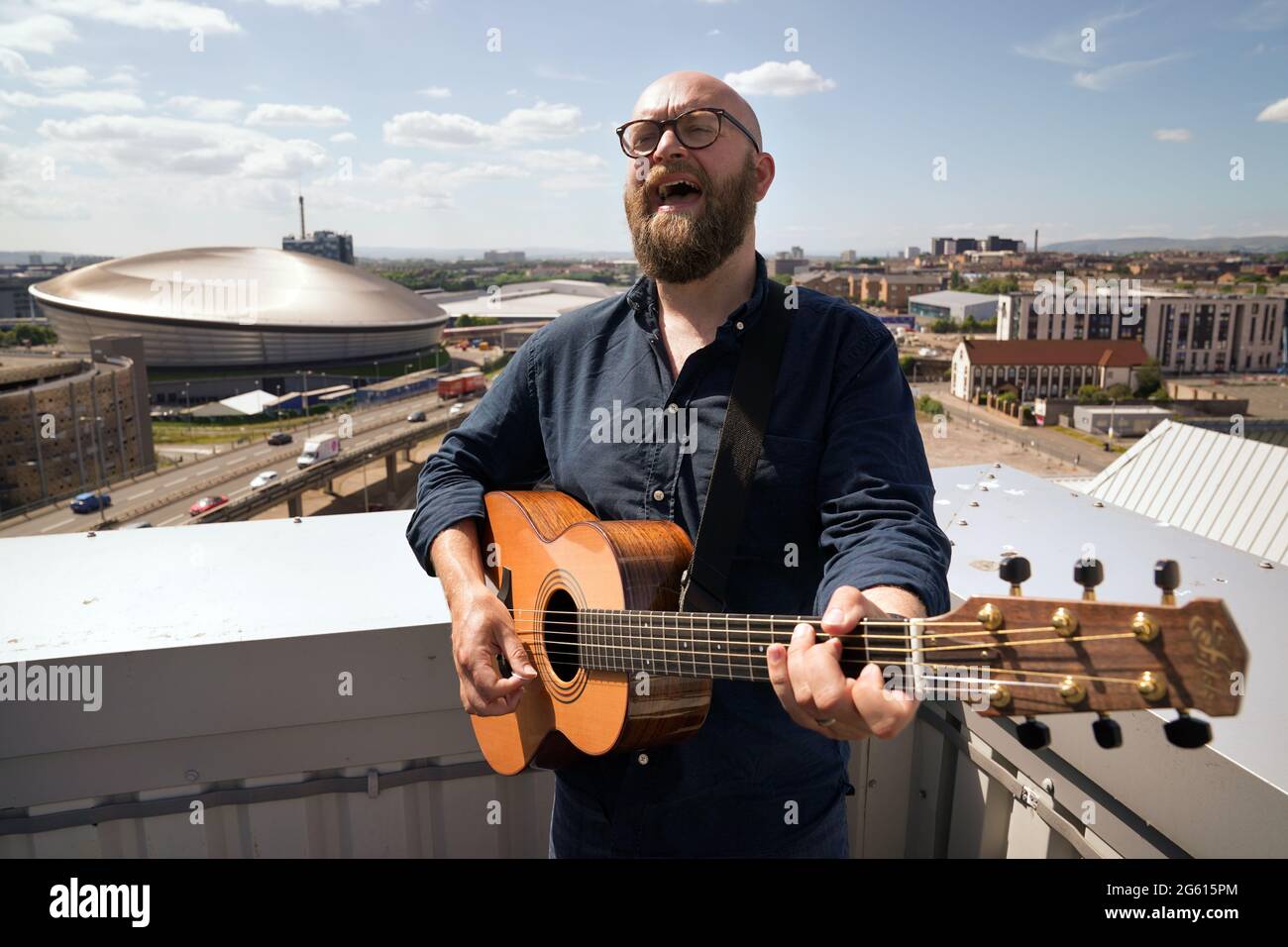 Il musicista Findlay Napier si esibisce sul tetto dello Skypark di Glasgow con il locale SSE Hydro come sfondo mentre si prepara a registrare le prime sessioni di musica Skypark con la band Mt. Dubbio, e il musicista Daniel Meade. Le sessioni saranno in streaming il 13,20 e 27 agosto per dare nuova esposizione musicale e materiale promozionale in un momento in cui i musicisti non sono stati in grado di suonare dal vivo. Data immagine: Giovedì 1 luglio 2021. Foto Stock