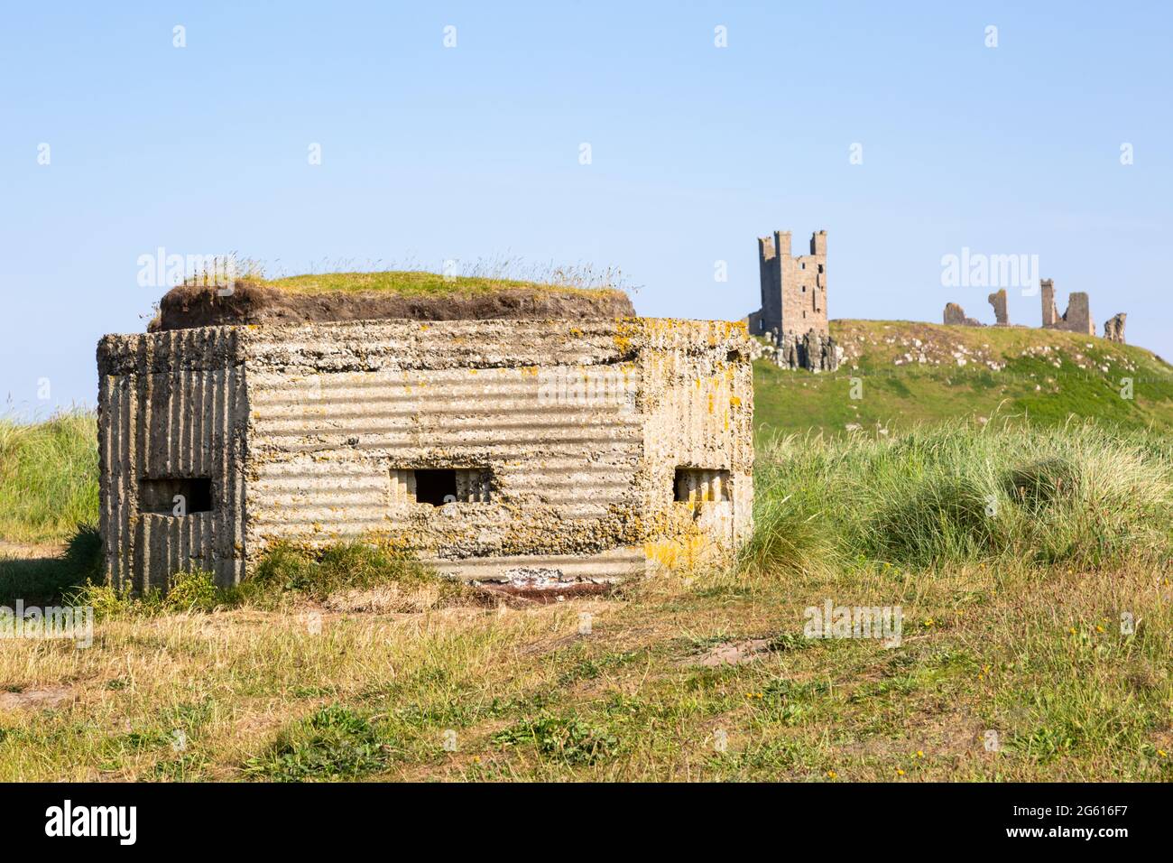 WW II pillbox sulla costa, con Dunstanburgh Castle in lontananza, Northumberland, Regno Unito Foto Stock