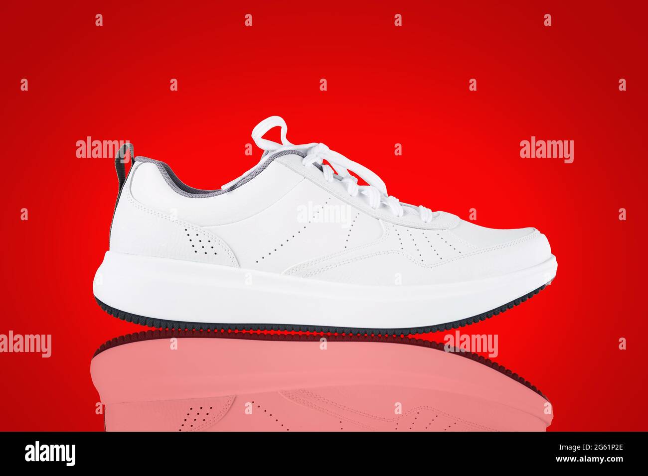 Nuova sneaker bianca isolata su sfondo rosso con riflessi. Primo piano delle scarpe sportive. Stile Street fashion Foto Stock