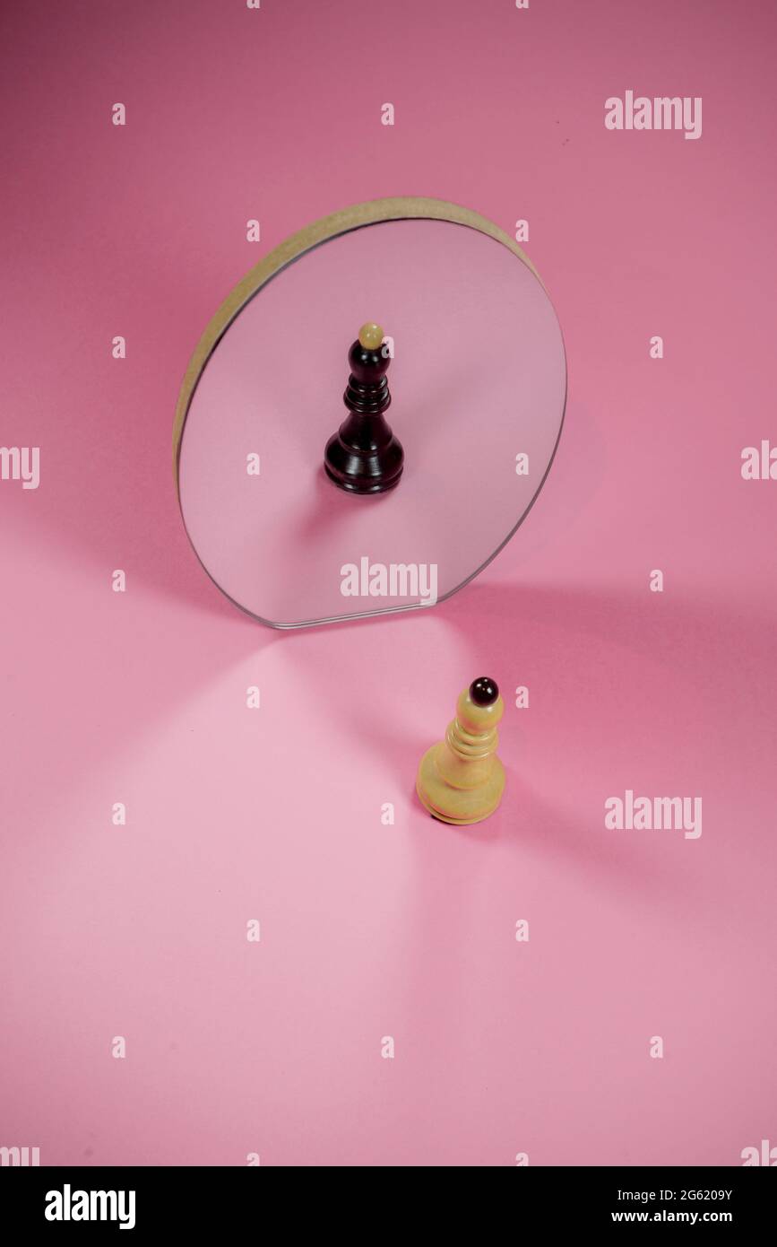 Scacchi pezzo bianco vescovo con riflesso nero in uno specchio. Su sfondo rosa pastello alla moda. Illusione ottica. Personalità diverse idea. Foto Stock