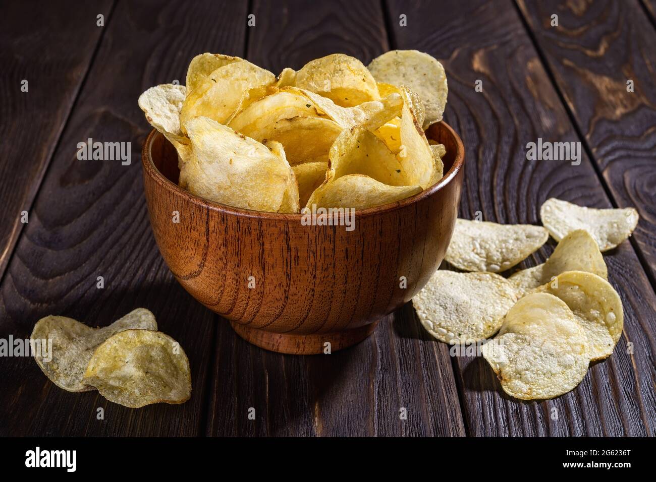 Patatine biologiche croccanti con aneto in una ciotola di legno marrone su un tavolo di legno nero. Spuntino croccante a fette di patate fritte. Fast food, cibo spazzatura. Foto Stock