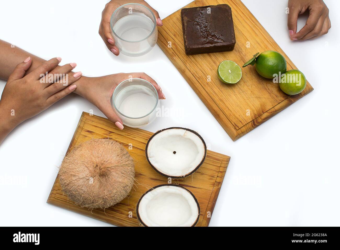 Le mani della donna tengono panela di canna da zucchero, limoni e noci di cocco su una tavola di legno su uno sfondo bianco. La citronella e l'acqua di cocco sono bevande tropicali Foto Stock