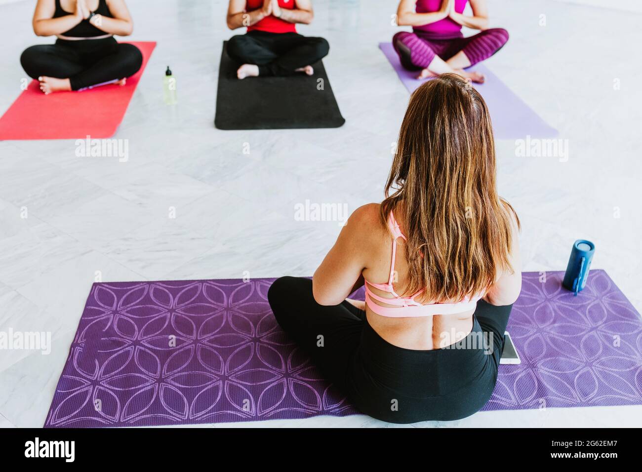 Donna ispanica seduta facendo yoga e meditazione in classe di gruppo in America Latina Foto Stock