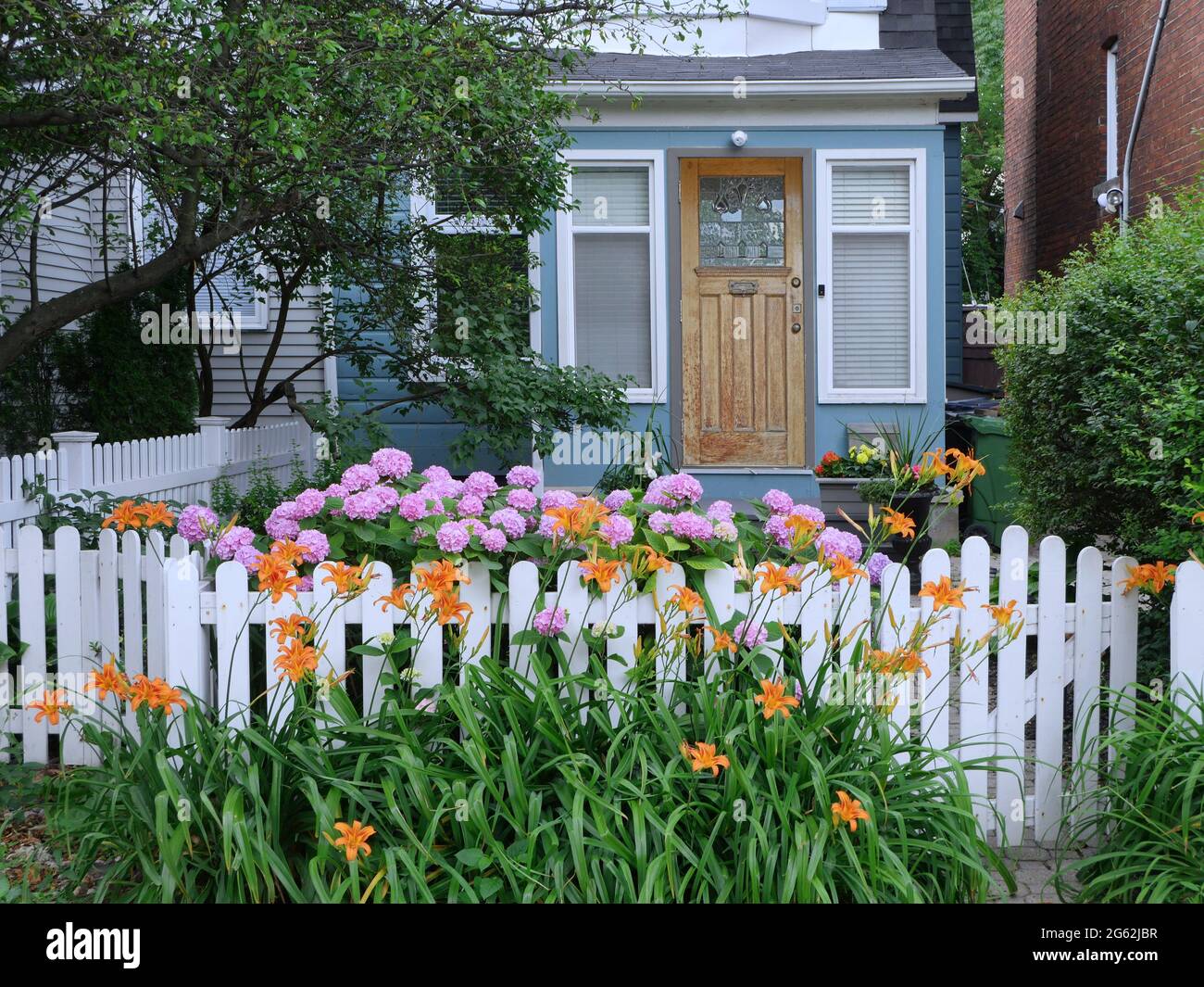 Affascinante piccola vecchia casa con recinzione bianca e fiori nel giardino di fronte Foto Stock