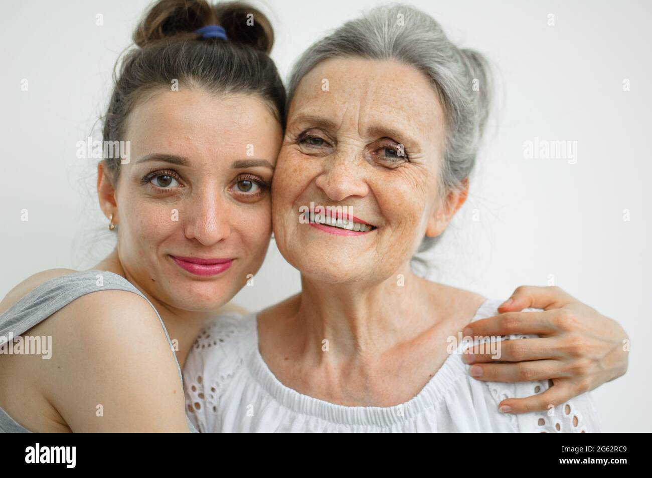 Felice madre anziana sta abbracciando la sua figlia adulta, le donne stanno ridendo insieme, famiglia sincera di diverse generazioni di età che si divertono sul bianco Foto Stock