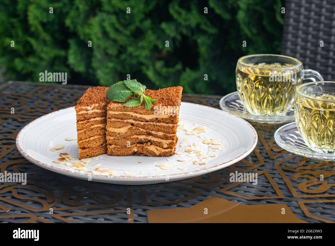 Pezzi di torta e due bicchieri di tè alla menta. Torta Medovik su un tavolo in un caffè estivo. Concetto di bevande a base di tè, cultura russa. Vita morta. H fatto in casa Foto Stock
