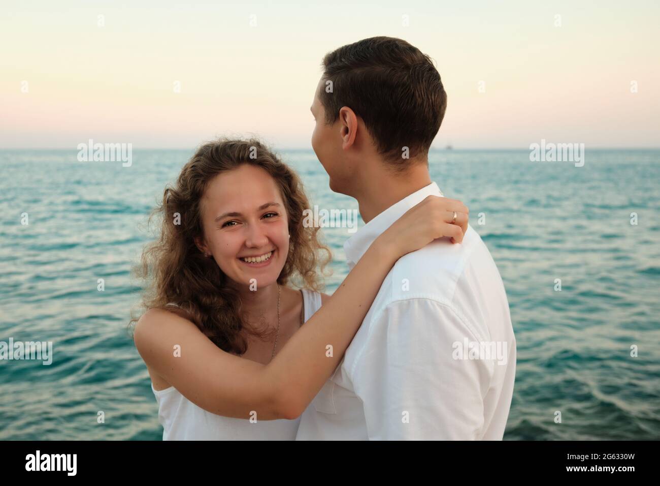 Donna abbraccia il suo amato uomo sorridente contro il tramonto sul mare Foto Stock