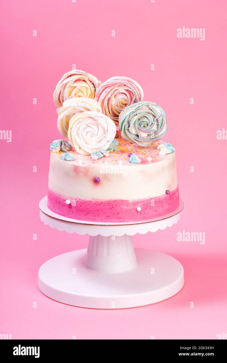 Torta di compleanno rosa e bianca decorata con meringa colorata. Dessert a colori con glassa per le vacanze dei bambini Foto Stock