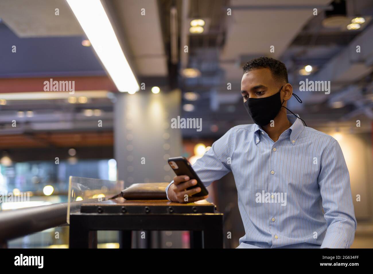 Ritratto di bell'uomo d'affari africano nero all'interno del centro commerciale con maschera facciale e telefono cellulare Foto Stock