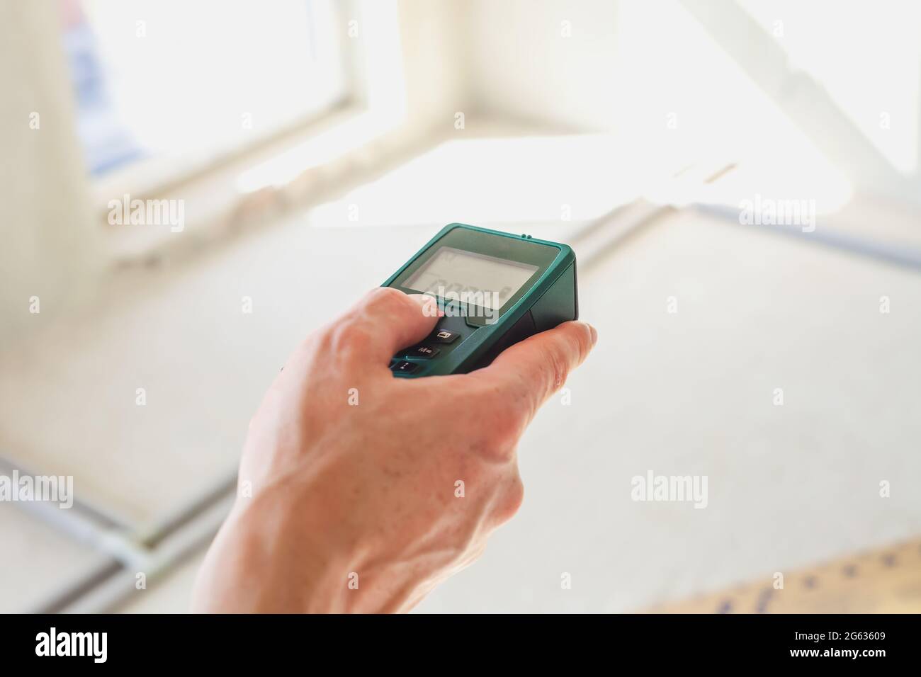 Telemetro laser in mano dell'uomo. Tecnico che tiene il misuratore di distanza laser. Primo piano dispositivo di misurazione in casa. Operatore che utilizza il telemetro elettronico su buil Foto Stock