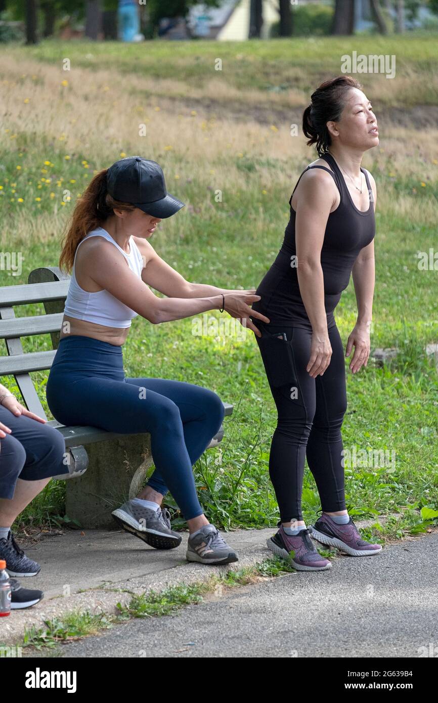Una donna che lavora con il suo addestratore sulla forma adeguata per gli esercizi profondi di piegatura del ginocchio. I un parco a Queens, New York City. Foto Stock