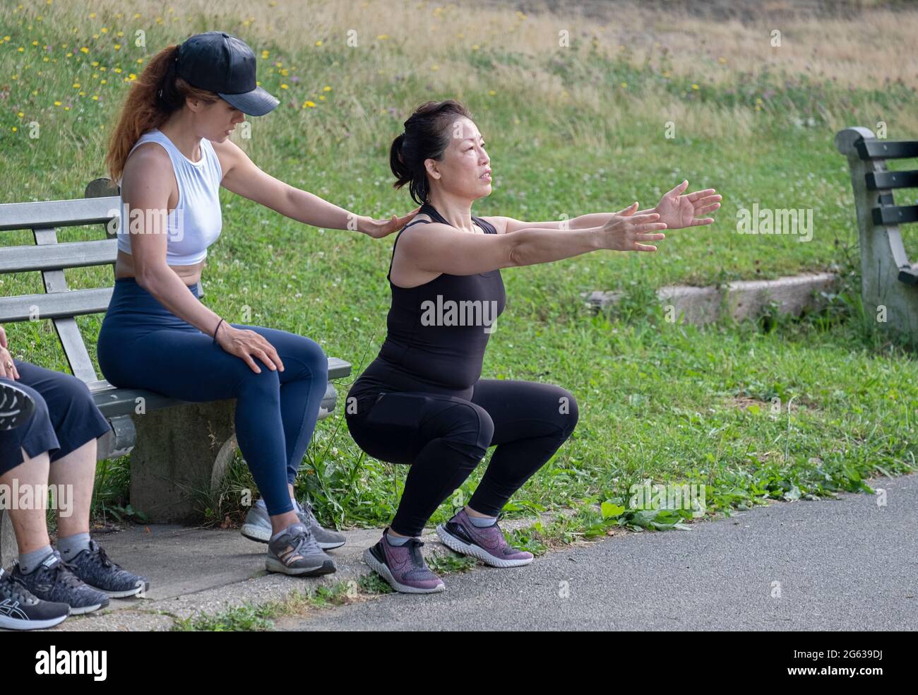 Una donna che lavora con il suo addestratore sulla forma adeguata per gli esercizi profondi di piegatura del ginocchio. I un parco a Queens, New York City. Foto Stock