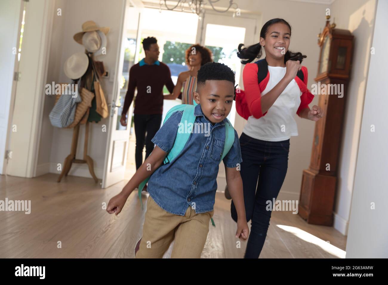 Felice coppia afroamericana con figlio e figlia di ritorno dalla scuola abbracciando e sorridendo a casa Foto Stock