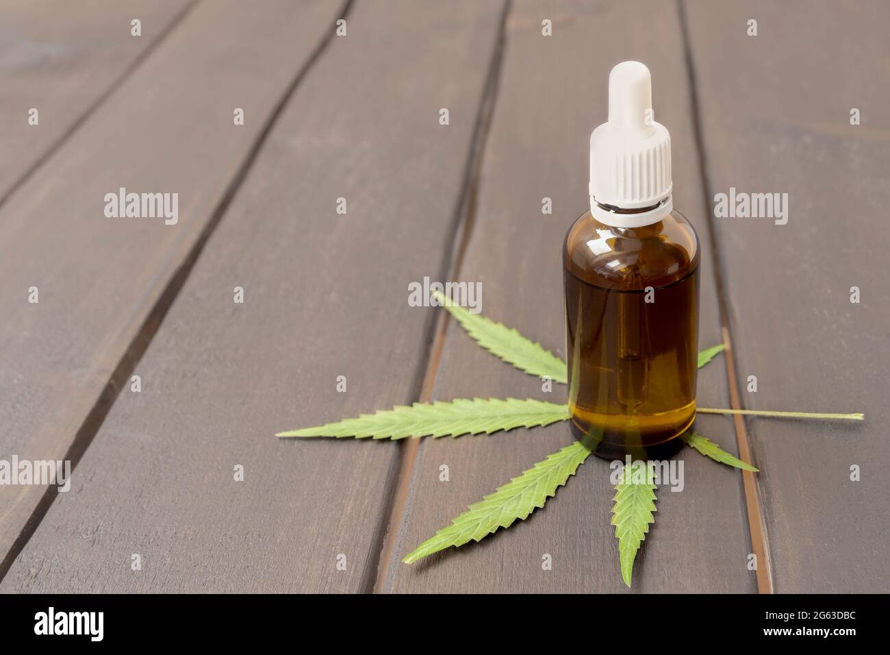 Bottiglia di vetro con dosaggio di gocce di erbe medicina organica olio CBD concentrato su sfondo di legno con foglia verde di marijuana, spazio di copia Foto Stock