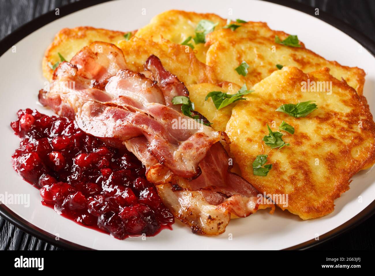 Frittelle di patate scandinave servite con marmellata di mirtilli e pancetta primo piano su un piatto sul tavolo. Orizzontale Foto Stock