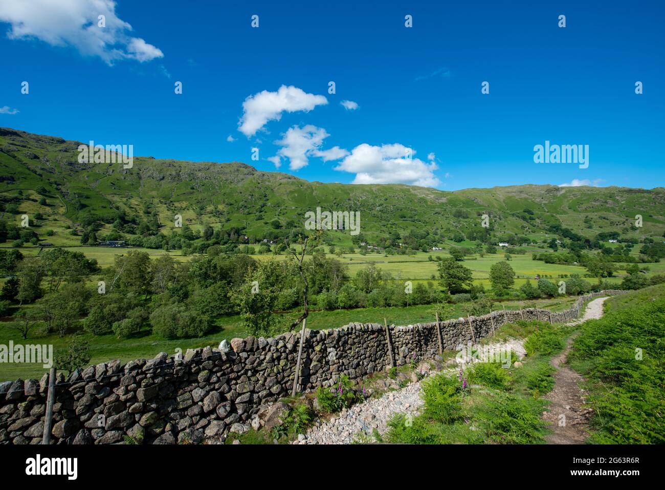 Guardando indietro lungo il sentiero nel Lake District con un cielo blu e muraglia in arenaria Foto Stock