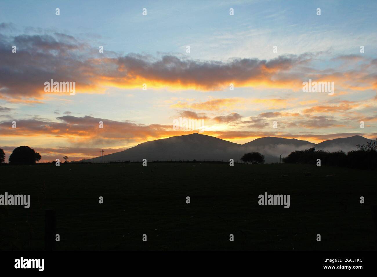 Splendido tramonto arancione dorato e nuvole su una montagna nella campagna di Pwlllheli, Galles del Nord Foto Stock