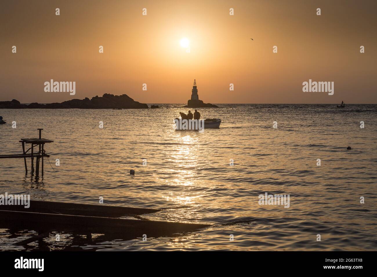 Ahtopol - 10 settembre: Sagoma di una barca con i pescatori di ritorno dalla pesca tra rocce e faro all'alba il 10 settembre 2016, Ahtopol Foto Stock