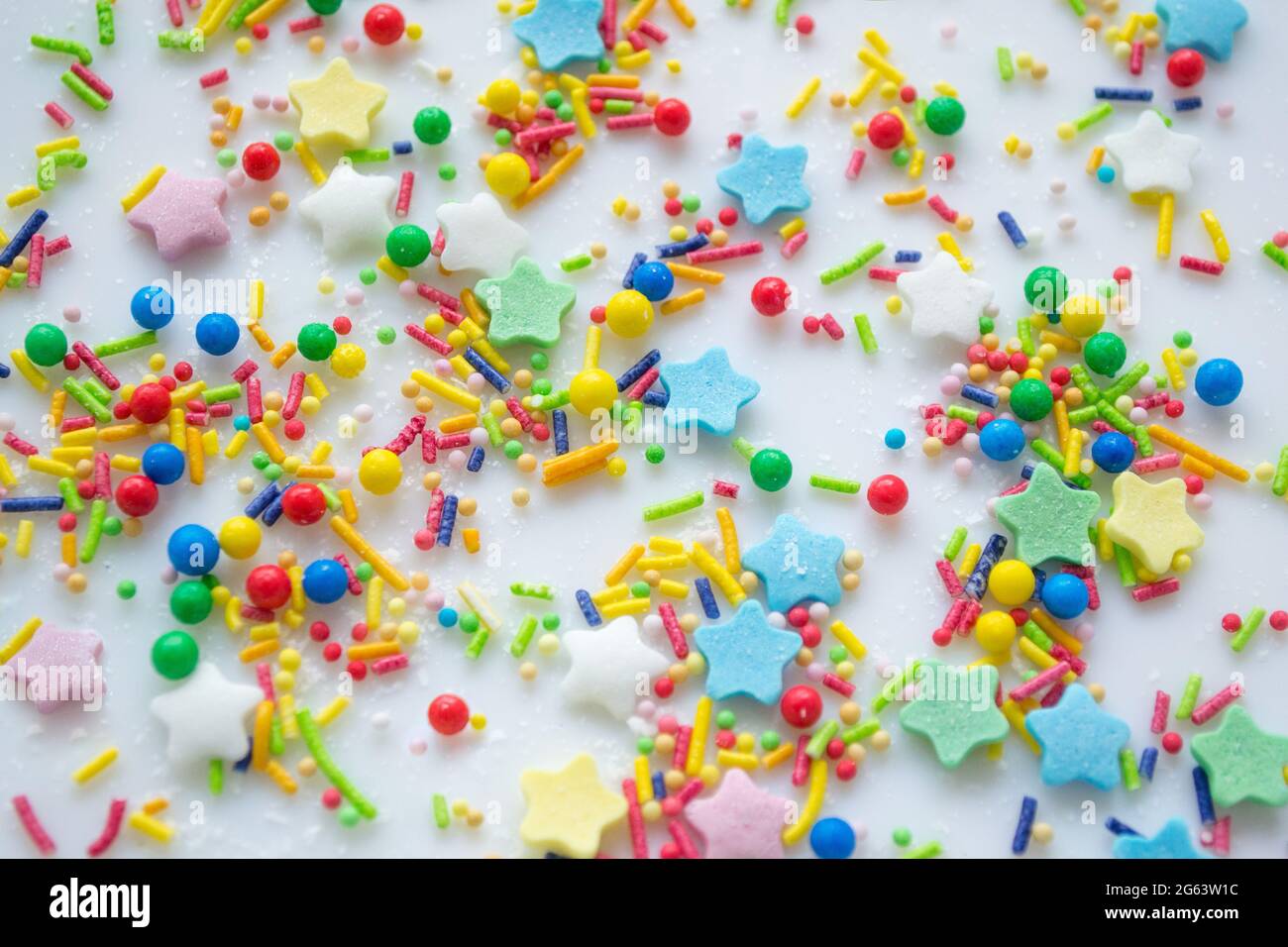 Sfondo festivo multicolore di una dispersione di caramelle zuccherate per cupcakes e altri dolci sotto forma di stelle, bastoni e palle. Colore pastello Foto Stock