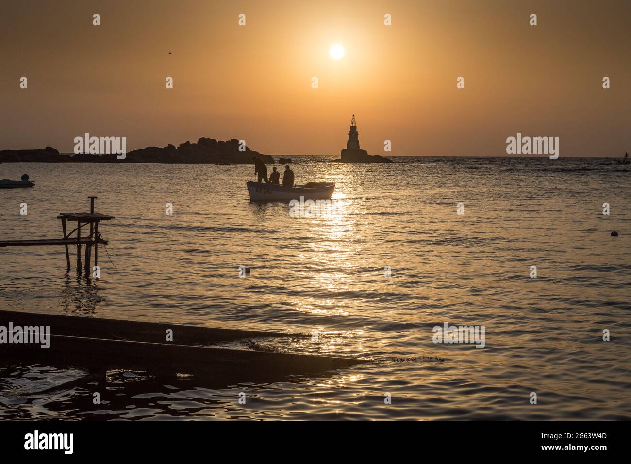 Ahtopol - 10 settembre: Sagoma di una barca con i pescatori di ritorno dalla pesca tra rocce e faro all'alba il 10 settembre 2016, Ahtopol Foto Stock