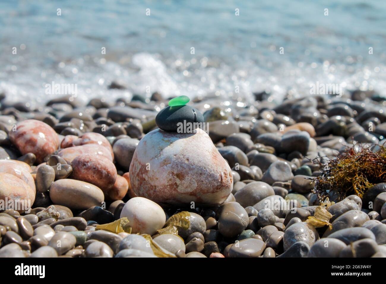 La piramide è costruita su una spiaggia di ciottoli di mare con un vetro verde satinato liscio in cima. Sullo sfondo di onde, schizzi d'acqua e. Foto Stock