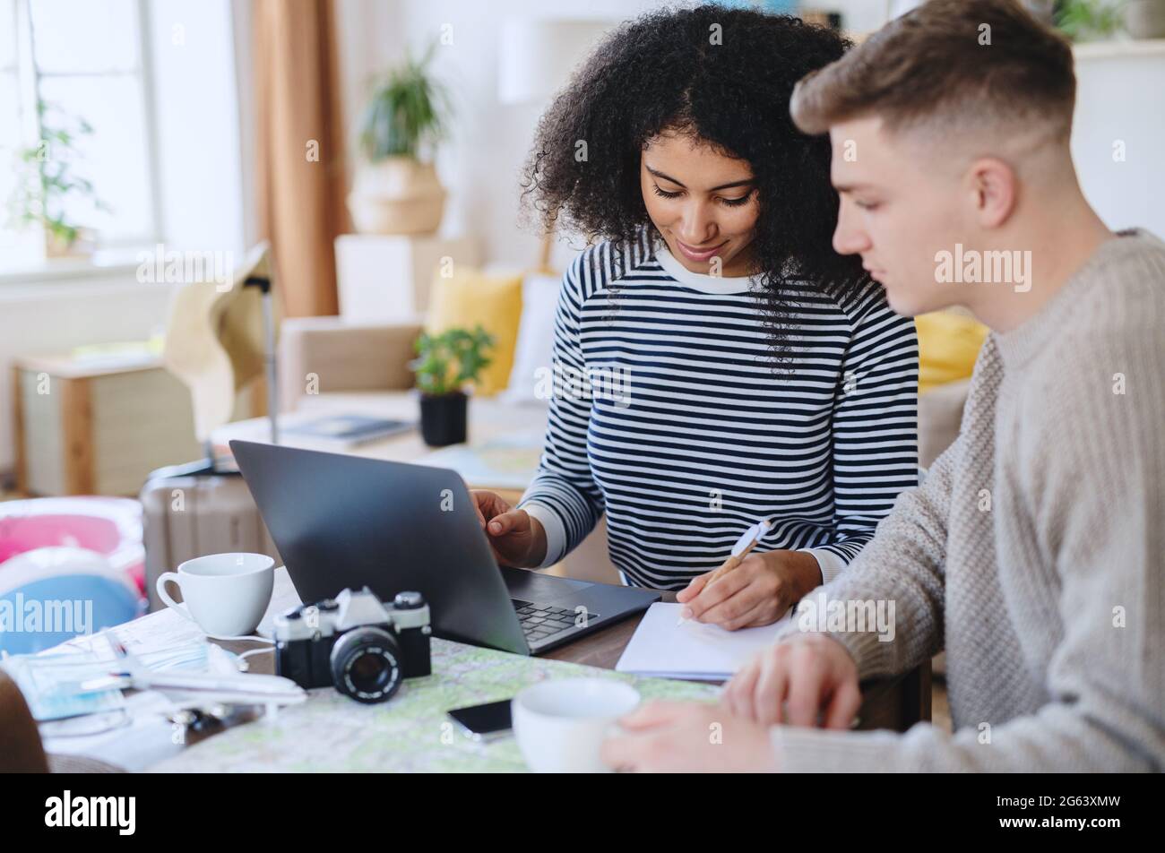 Giovane coppia con lmap e laptop pianificazione vacanza, coronavirus e nuovo concetto normale. Foto Stock