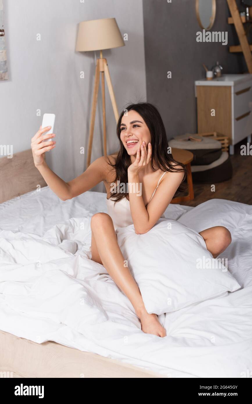 giovane donna allegra che si stacca la lingua e prende selfie mentre si  siede sul letto Foto stock - Alamy